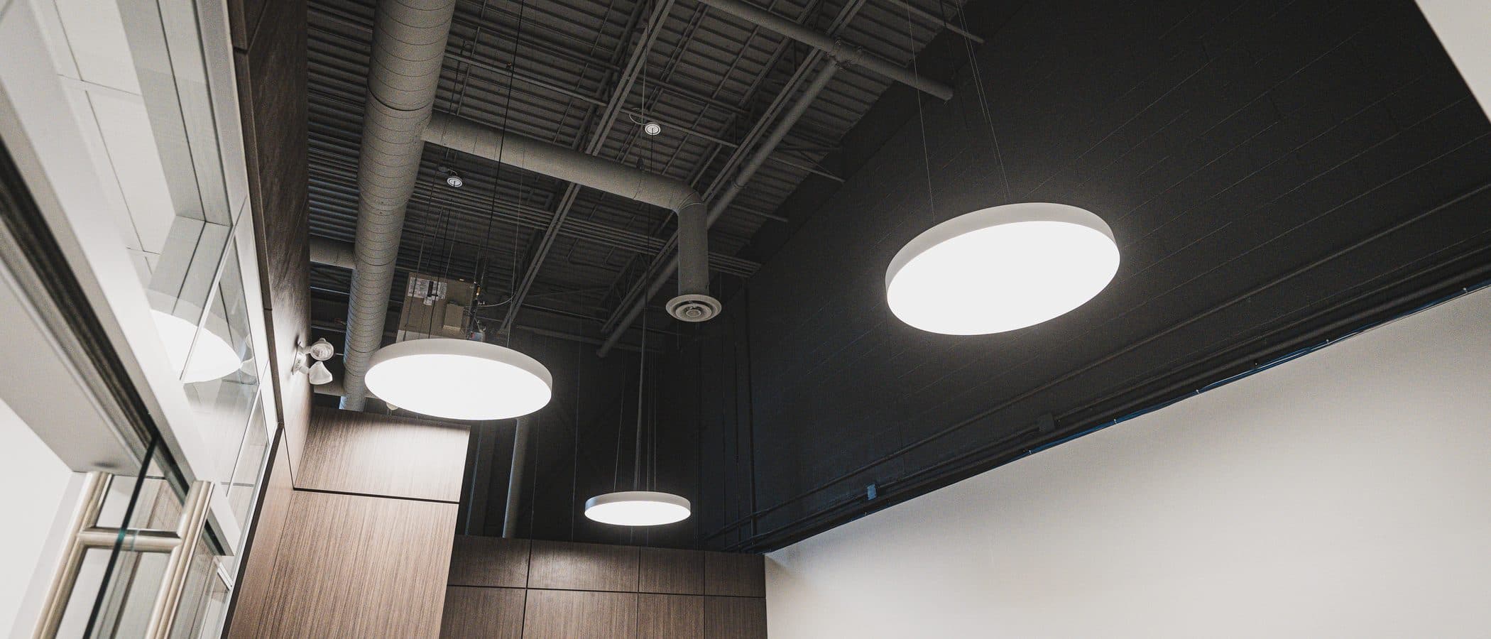 Pendant drum lights and exposed ductwork above a walnut millwork corner with two doors set into the paneling.