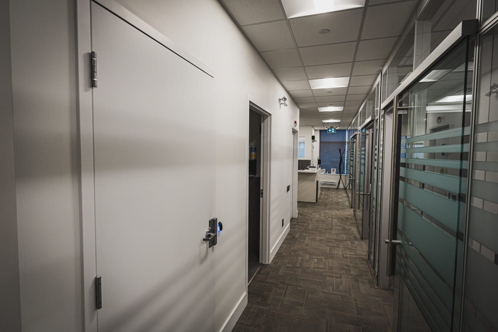 Long interior hallway with glazed office fronts on one side leading toward a distant reception area.