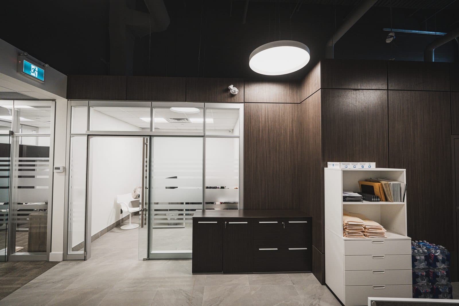 Small glass fronted meeting room with a dark wood credenza beneath pendant lighting and a striped privacy film door.