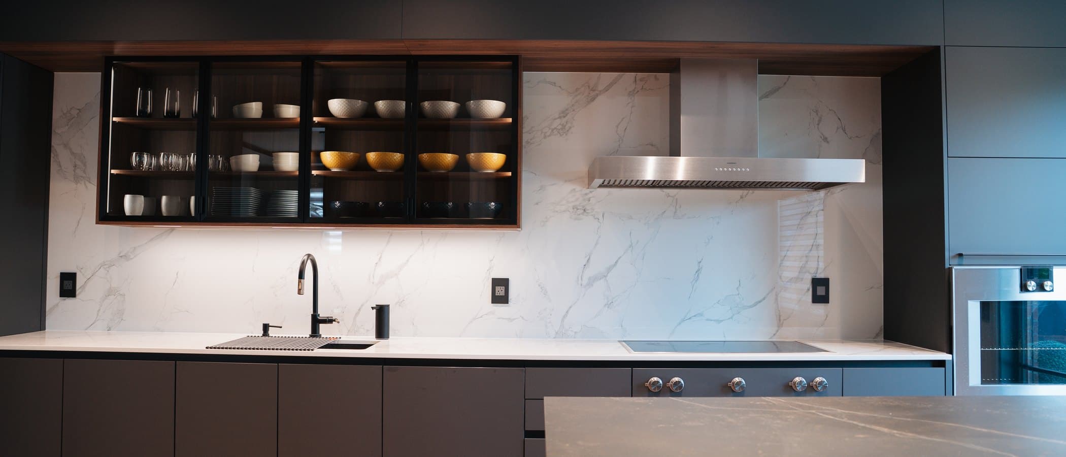 Kitchen in charcoal cabinetry with backlit display shelving and herringbone floors
