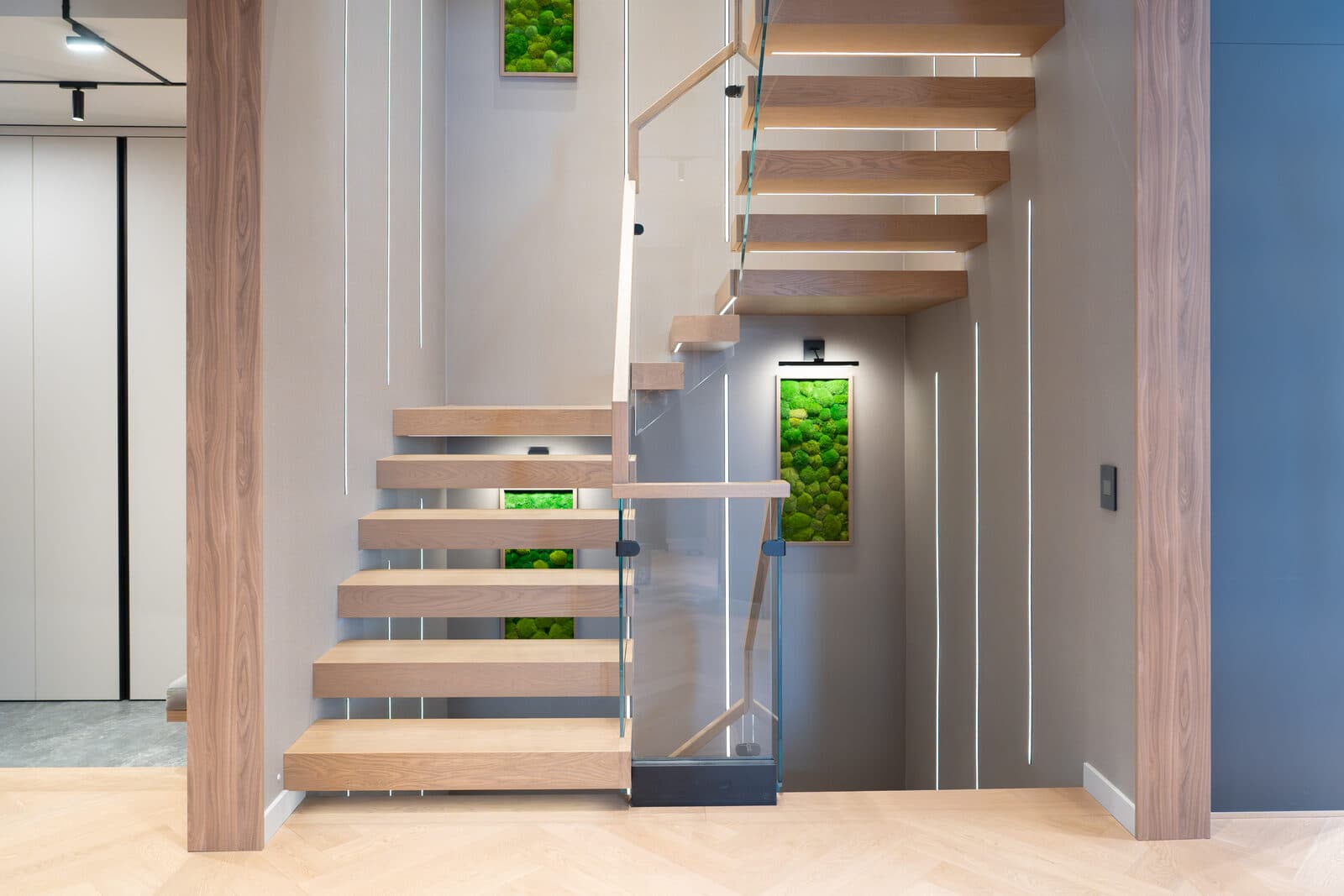 Floating oak stair with backlit moss panels and concealed lighting at the entry
