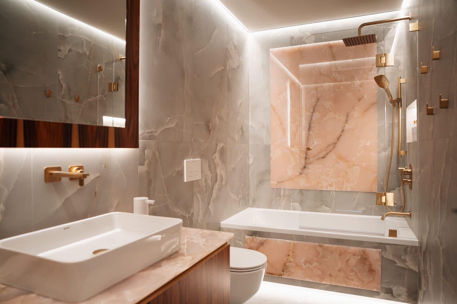 Pink onyx bathroom with a layered vanity, backlit mirror and freestanding tub