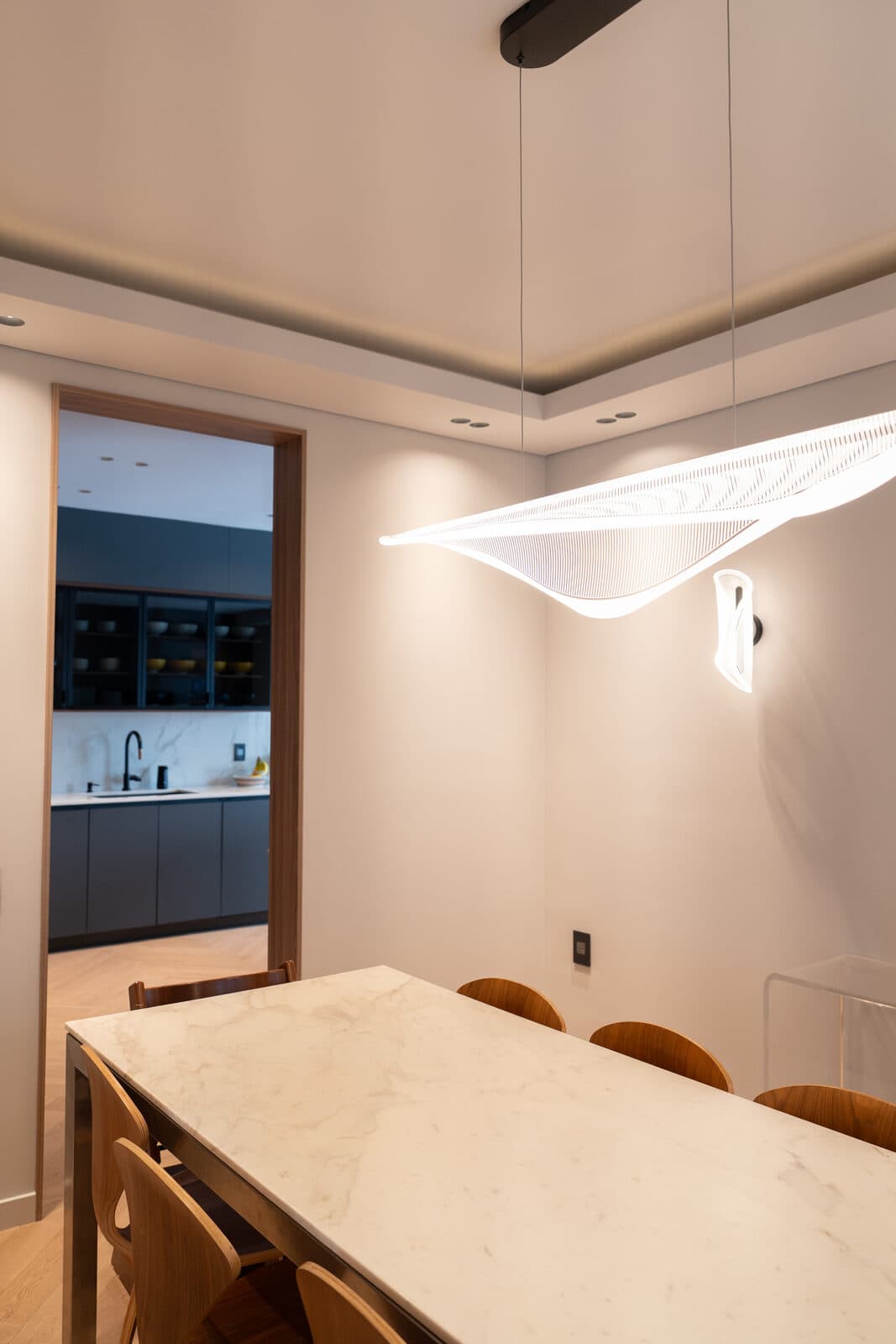 Dining room with a sculptural winged pendant over a marble table and the kitchen beyond