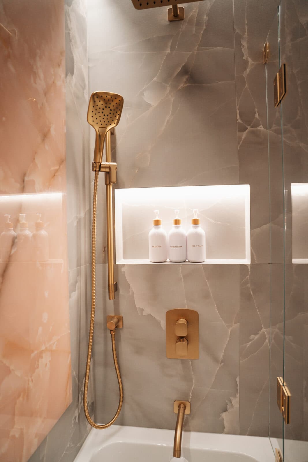 Onyx shower with a gold rain head above a lit stone niche
