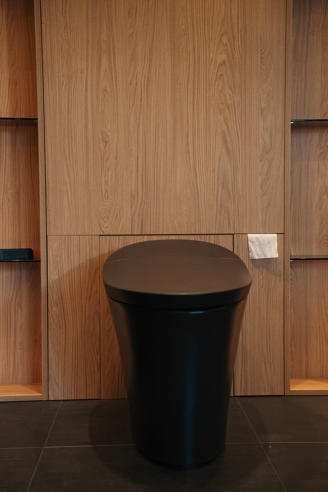Floating toilet set into a wood lined niche in the black bathroom