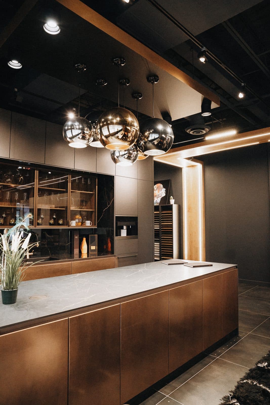 Display kitchen in walnut and stone lit by chrome globe pendants
