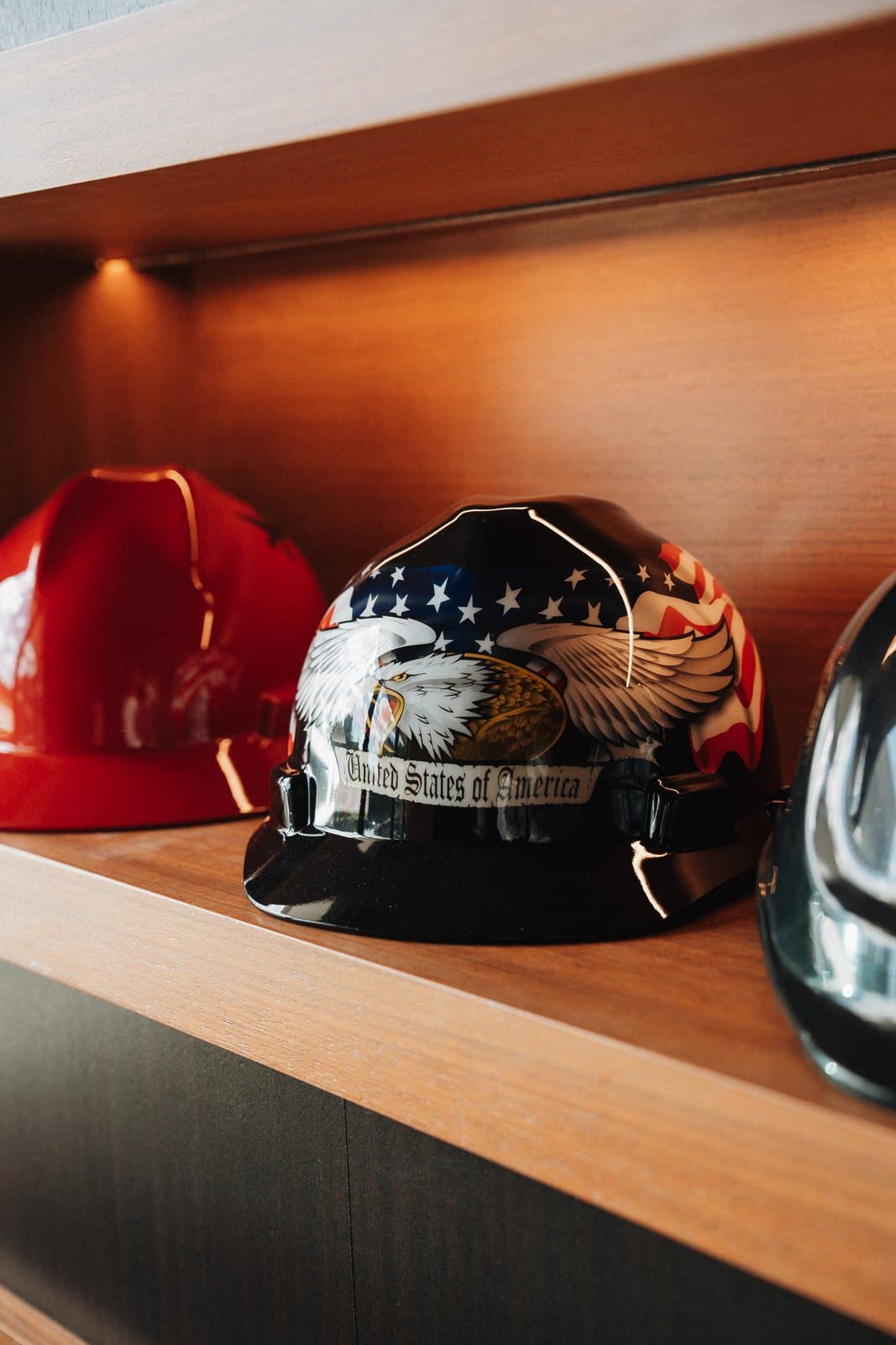 Hand painted hard hats displayed on backlit oak shelving as a craft tribute