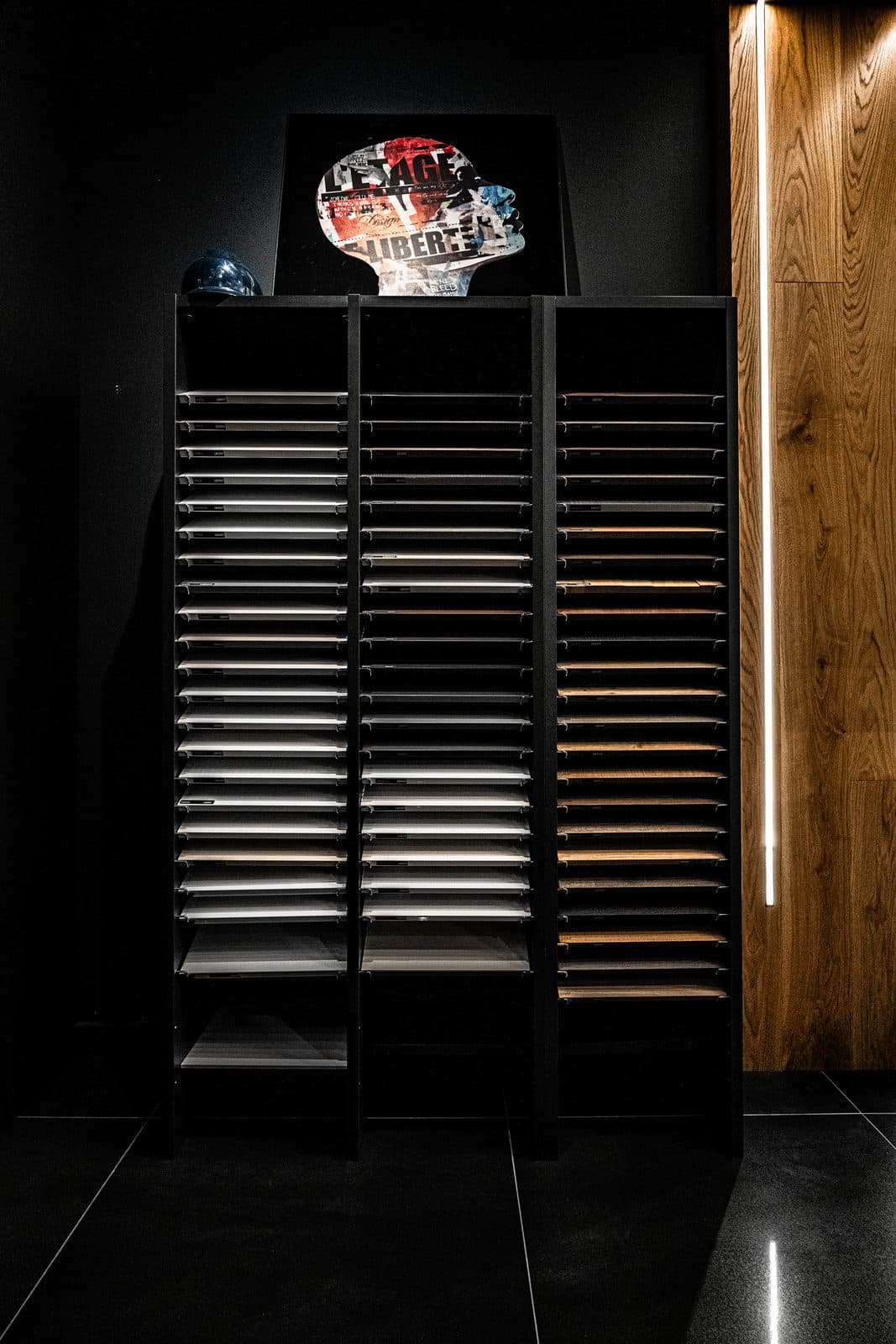Illuminated finish sample tower displaying wood, stone and fabric swatches beside a raw timber slab wall