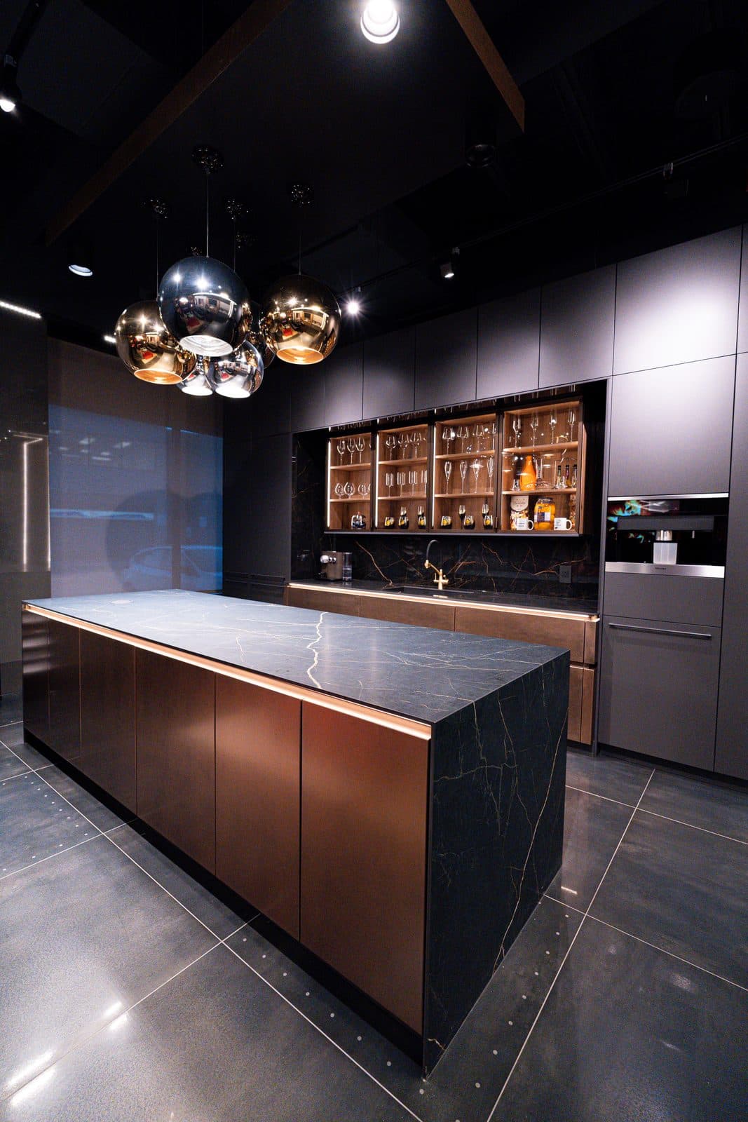 Bronze display kitchen with mirrored globe pendants, a glass wine cabinet and a waterfall marble island
