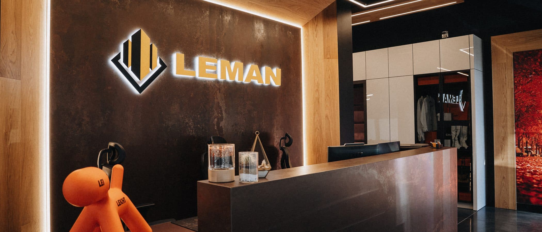 Reception desk beneath the illuminated Leman sign with a sculptural mascot and a merchandise display closet beyond