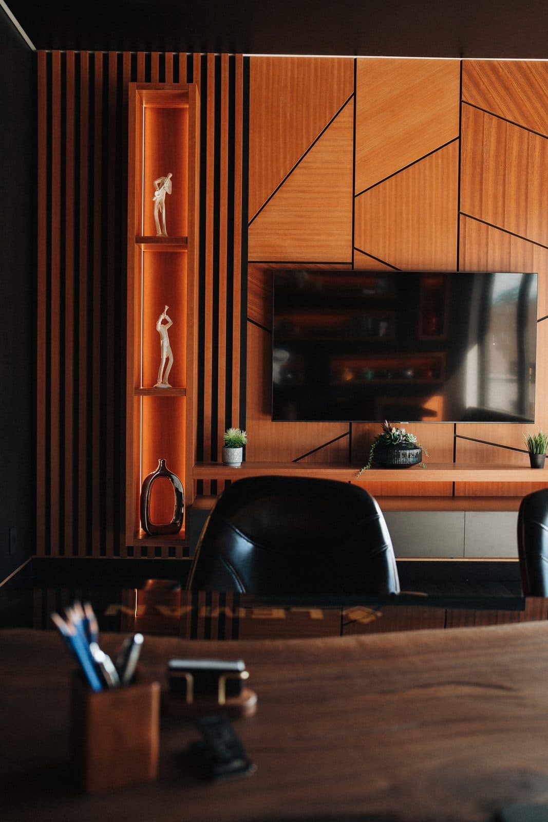 Private office with a geometric wood feature wall, a wall mounted screen and an illuminated display niche