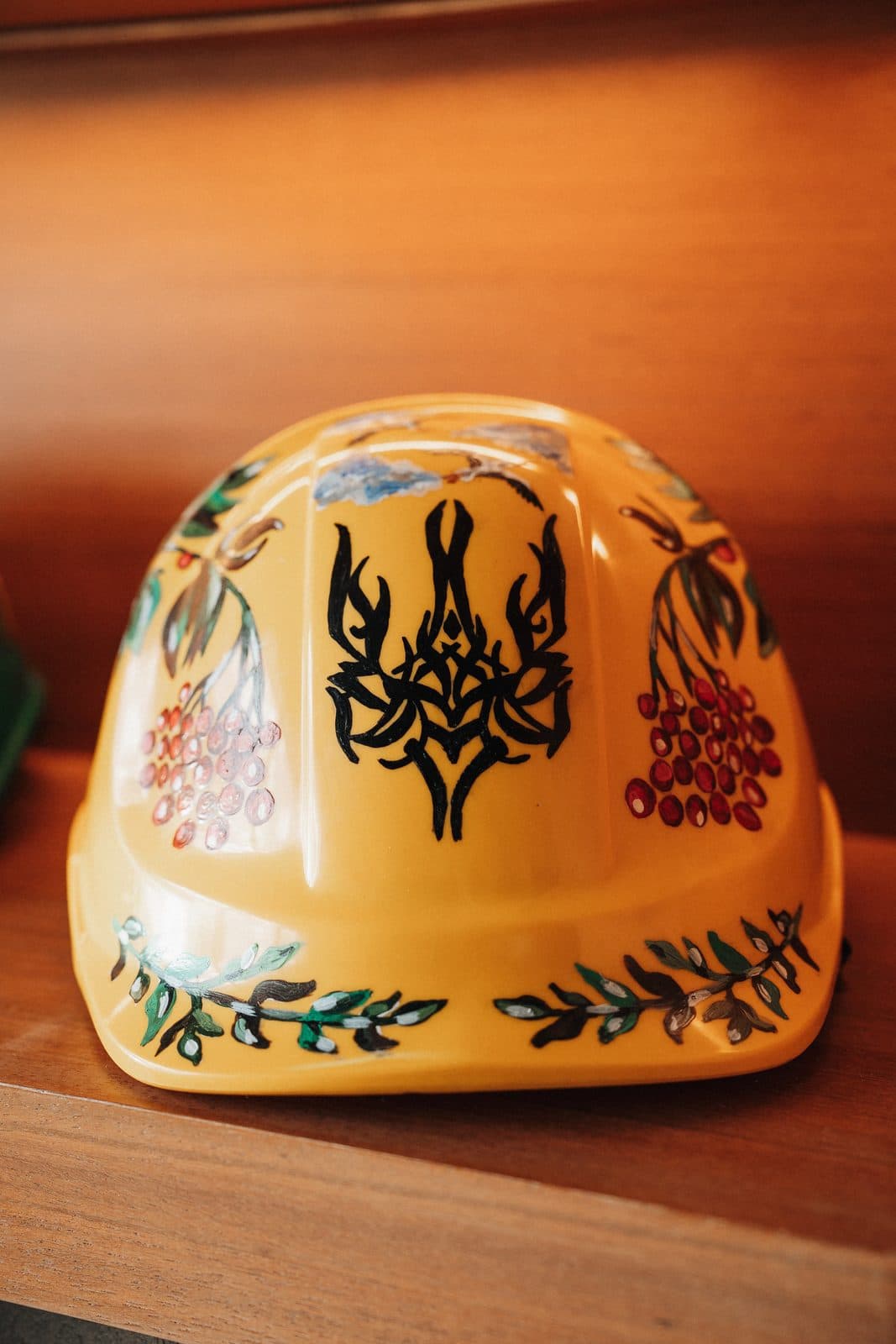 Hand painted hard hat with folk floral motifs displayed on backlit oak shelving