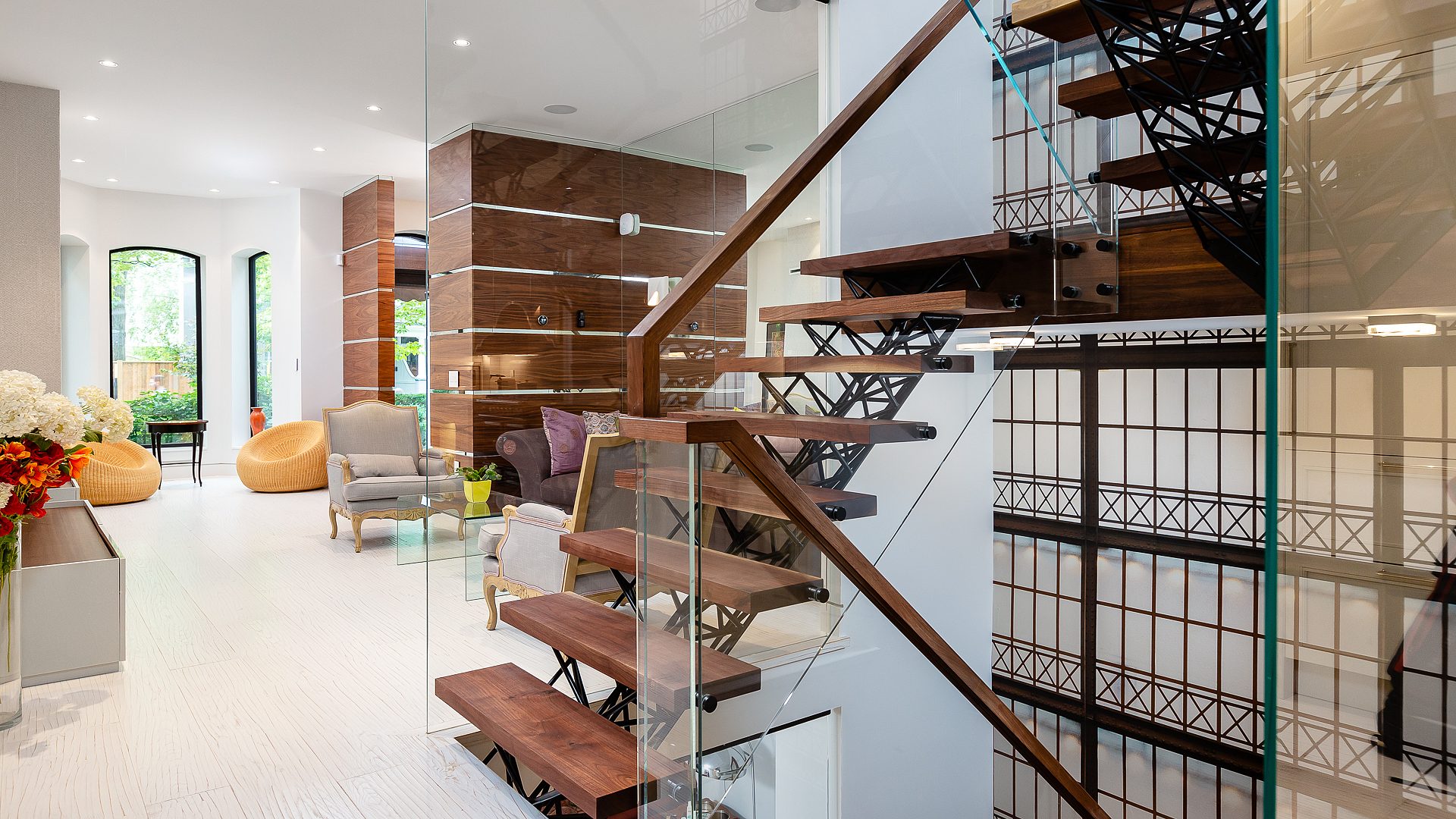 Floating walnut stair treads beside a custom iron screen opening the entry walk