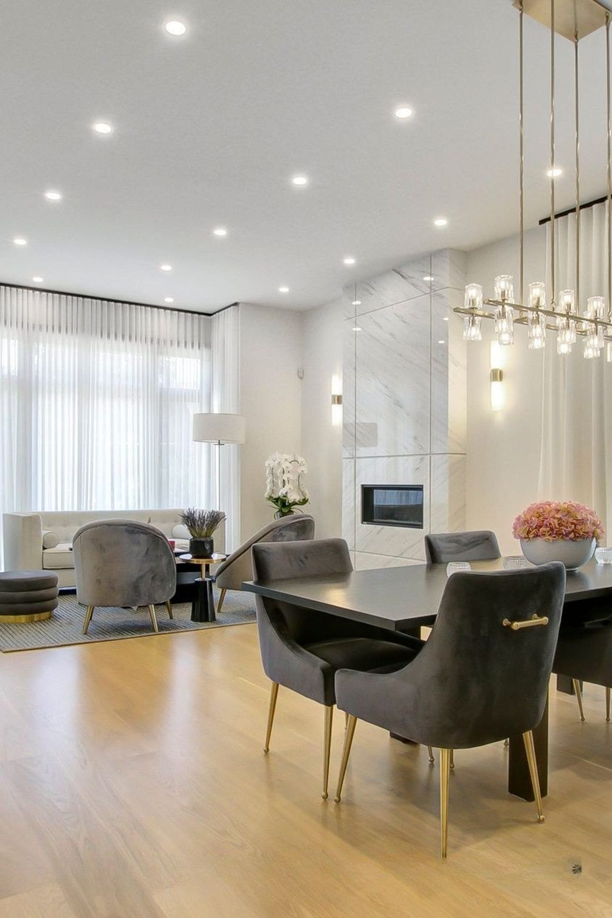 Open living and dining space with a slab marble fireplace and a linear brass chandelier